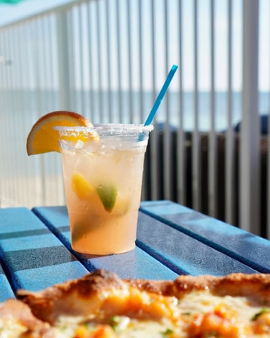 Beachside cocktail and pizza on a blue table with Gulf water in the background
